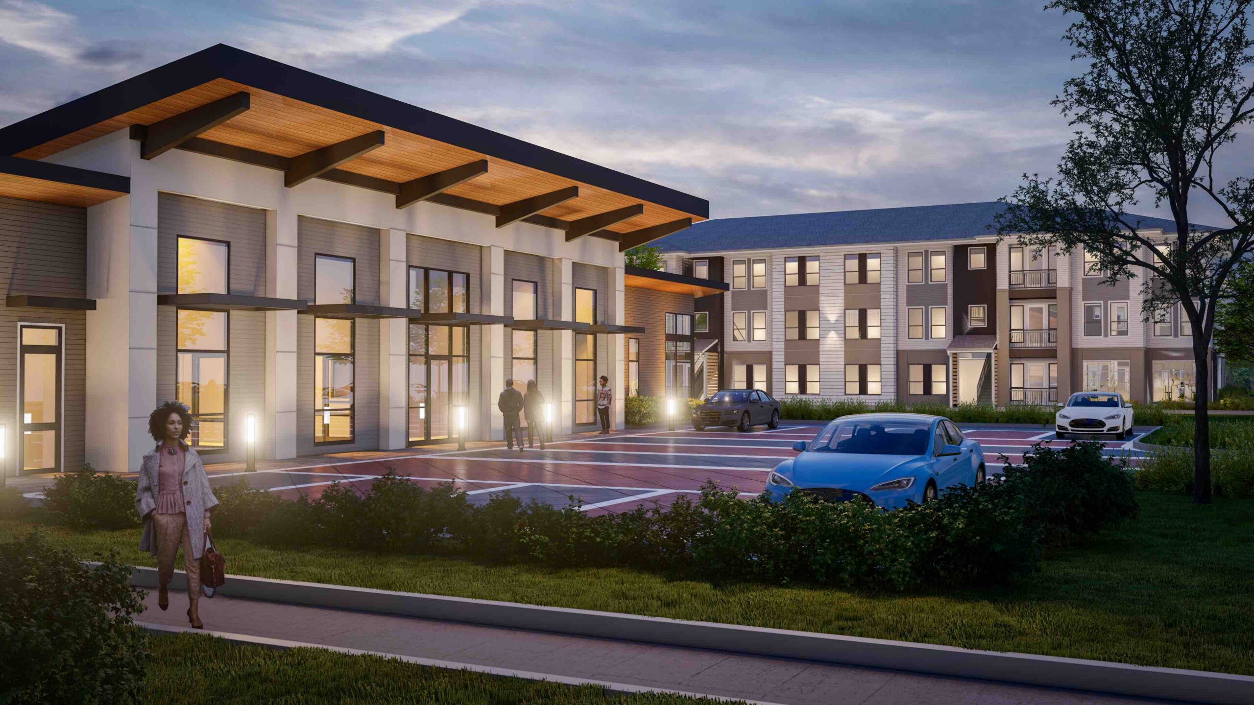 Modern apartment complex with exterior lighting, several parked cars, a few people walking near the entrance, trees, and well-maintained landscaping at dusk.